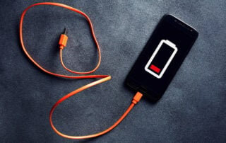 Smartphone avec logo de batterie vide sur l'écran, branché à un connecteur de charge